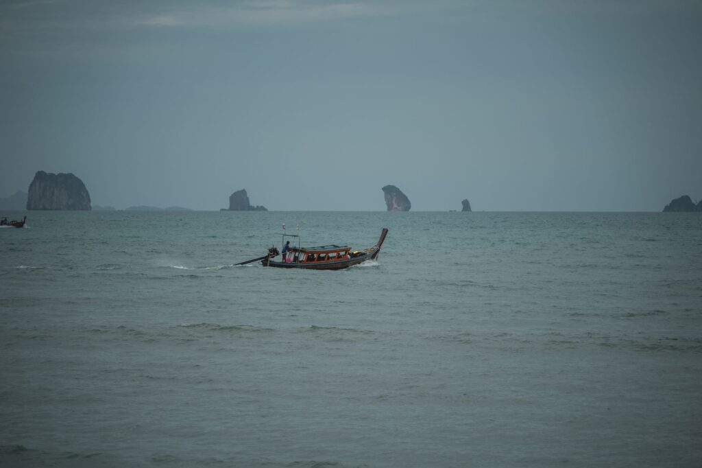 A traditional boat sails on a peaceful sea with distant rocky islands.