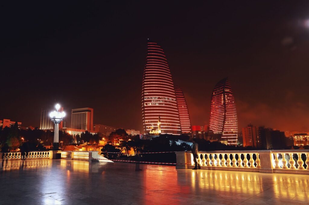 Dramatic night view of Baku's Flame Towers with glowing red lights, reflecting the urban cityscape.