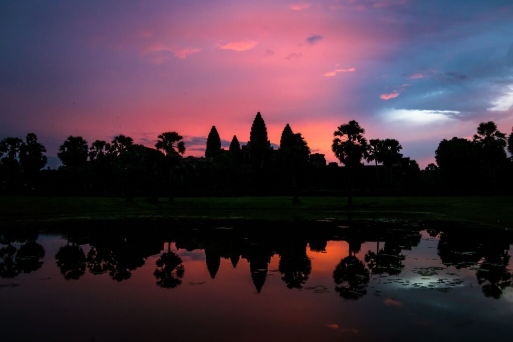Stunning silhouette of Angkor Wat with a vibrant sunset reflecting in the surrounding water.