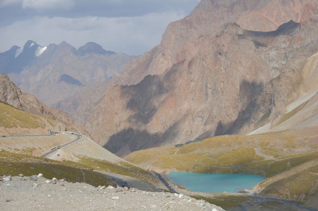 Scenic view of a mountain road with a stunning turquoise alpine lake and rocky terrain.