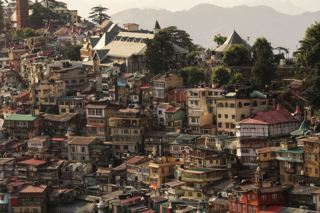 Aerial view of the bustling cityscape of Shimla, India, with colorful buildings and lush hills.