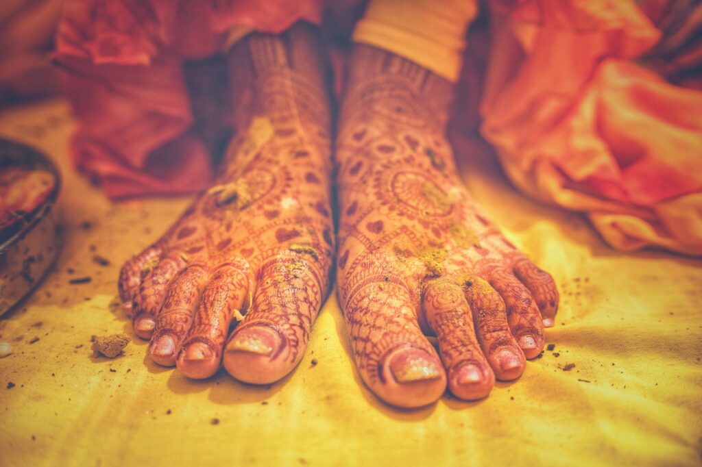 Close-up of henna decorated feet of a bride at an Indian wedding in Mussoorie, India, on yellow fabric.