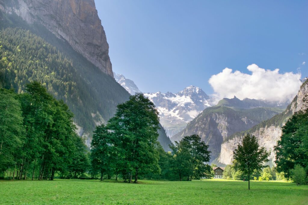 Stunning Alpine scene with lush green valley, towering peaks and blue sky with clouds.