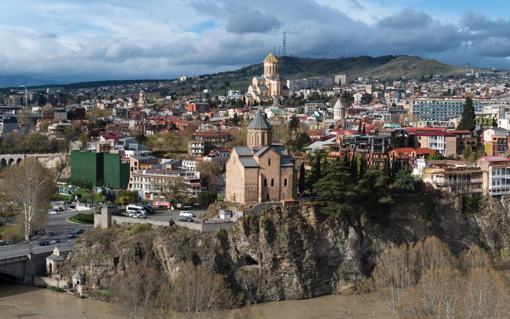 A panoramic view of Tbilisi, Georgia featuring historic churches and diverse architecture under a dramatic sky.