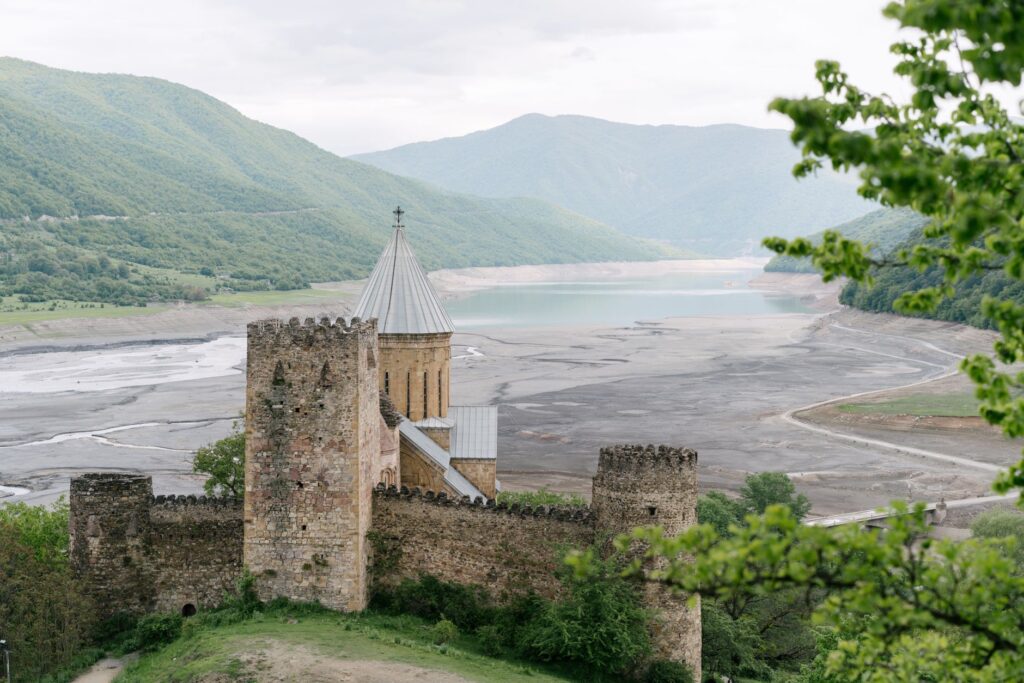 A stunning medieval castle overlooks a vast reservoir among lush green hills.