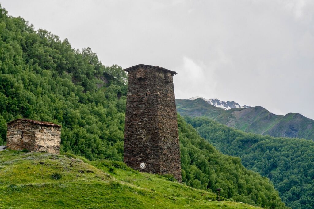 Stone tower in Mestia, Georgia amidst lush green hills and mountains.