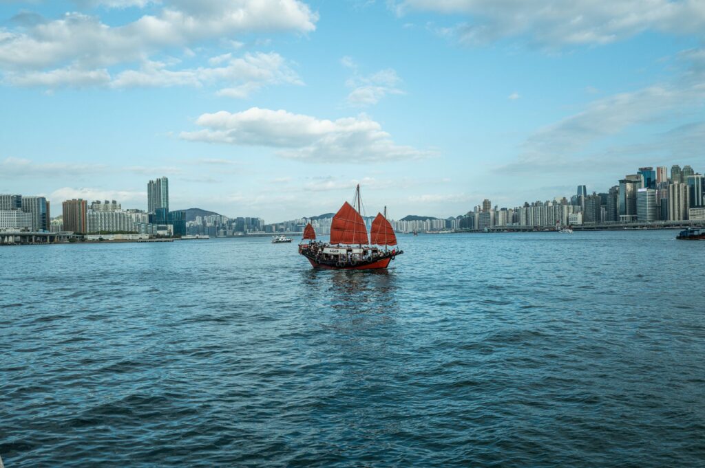 A traditional red-sail junk boat sails across the scenic Victoria Harbour in Hong Kong.