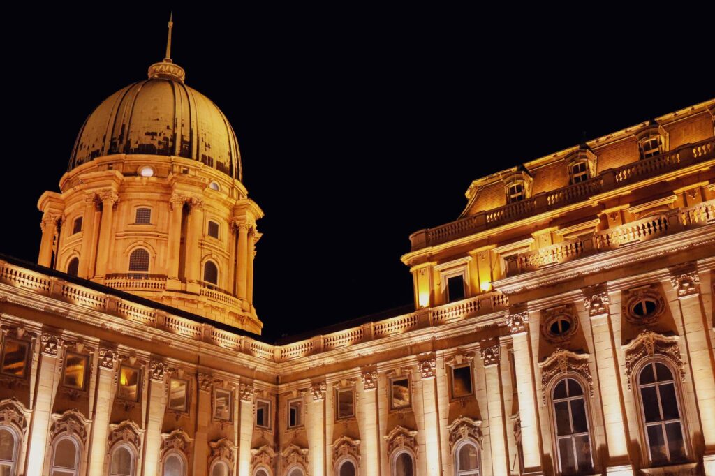 Illuminated Buda Castle dome and facade at night in Budapest, Hungary, showcasing Baroque architecture.