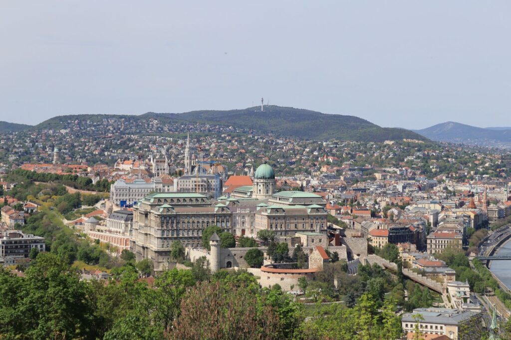 Scenic aerial view of Budapest featuring the iconic Buda Castle and surrounding cityscape under a clear sky.