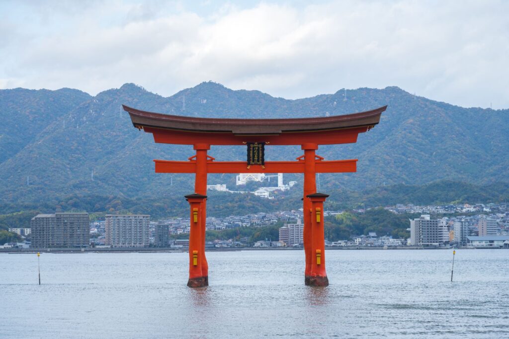 Scenic view of the floating Torii gate at Itsukushima Shrine in Japan, with mountains and sea.