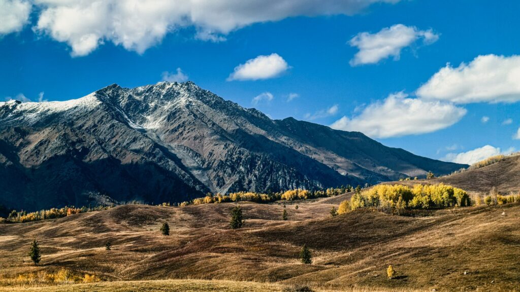 A breathtaking view of snow-capped mountains surrounded by autumn foliage under a clear blue sky.