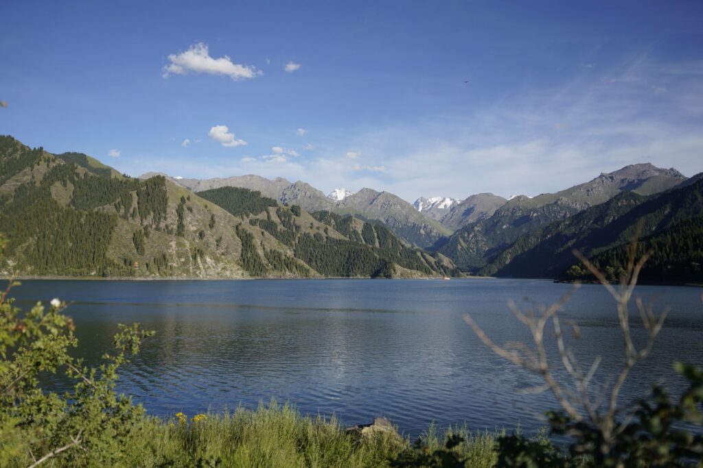 Stunning landscape of Tian Shan mountains with a tranquil lake under a clear blue sky.