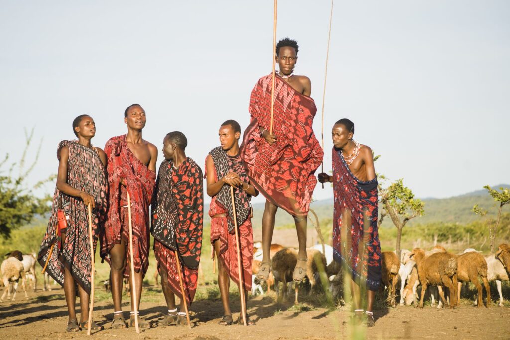 Young Maasai men in Tanzania jumping in traditional attire amidst a goat herd.