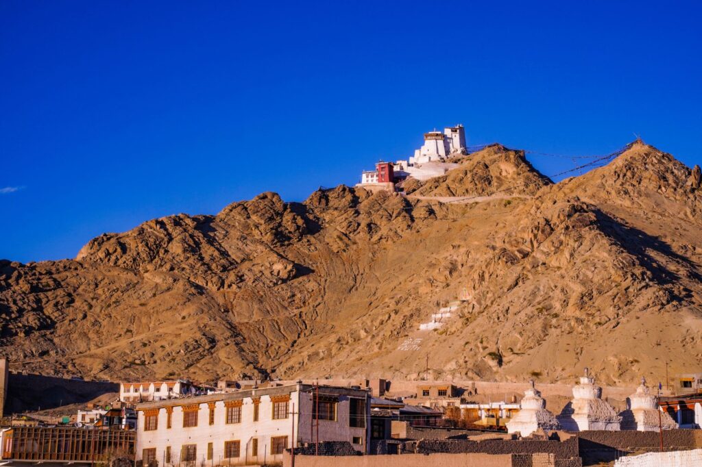 Picturesque view of a monastery atop a hill with clear blue skies in a rugged landscape.