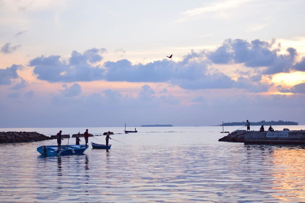 Fishermen in boats at dusk in the Maldives, surrounded by calm sea and vibrant skies.