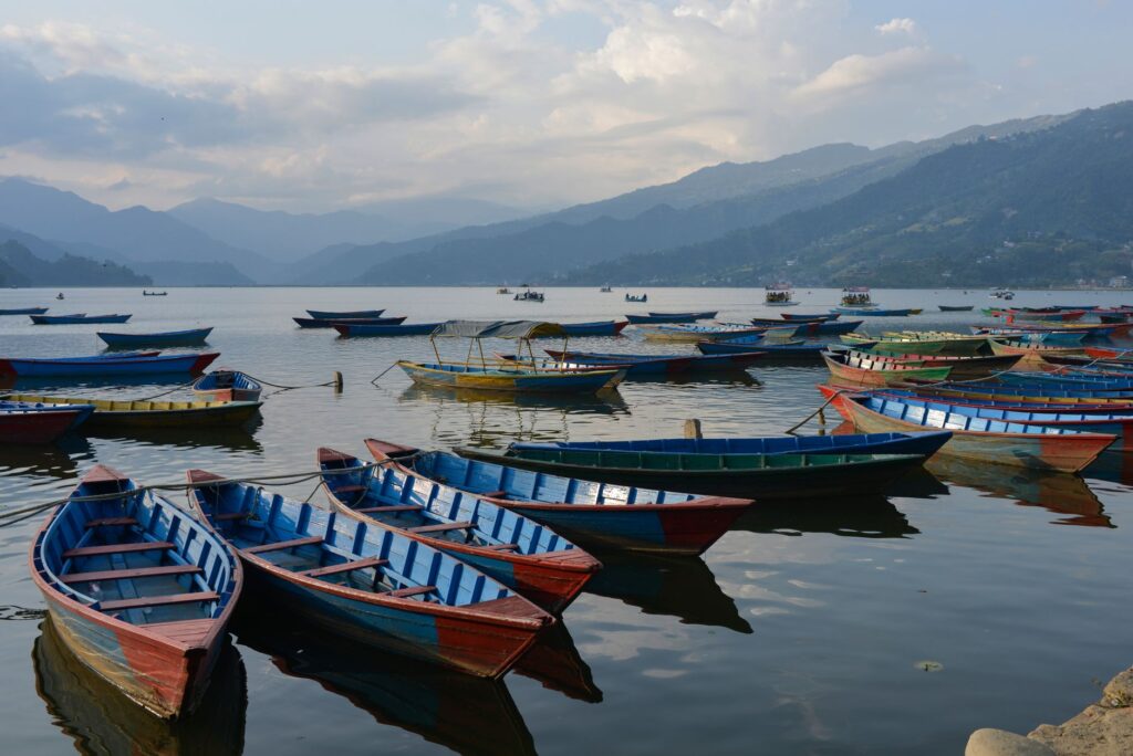 Scenic view of traditional wooden boats on Phewa Lake, with the Annapurna mountain range in the background during sunset.
