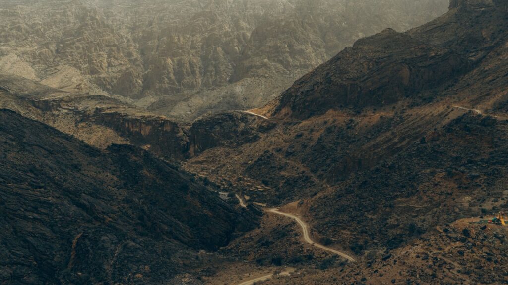 Stunning aerial view of Oman's rugged mountains, showcasing dramatic canyons and winding roads.