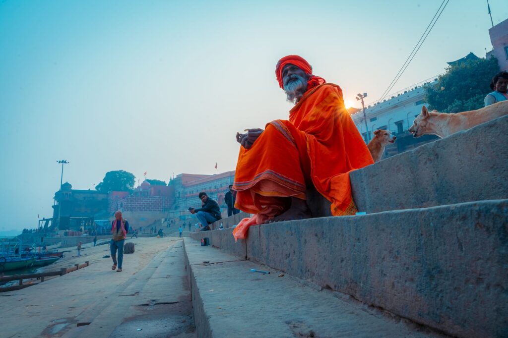 A holy man sits on the steps of Varanasi Ghats with the morning sun rising behind him, capturing the spiritual essence.