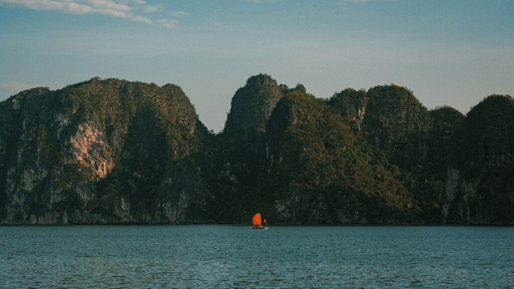 Serene image of limestone mountains with a small boat on tranquil water under a blue sky.