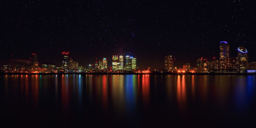 City skyline at night with shimmering water reflections and starry sky.