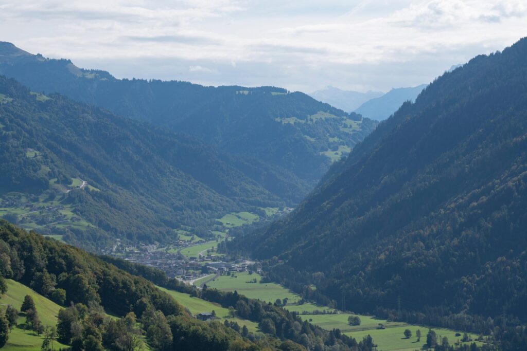 A breathtaking view of a lush green valley surrounded by towering mountains under a bright sky.