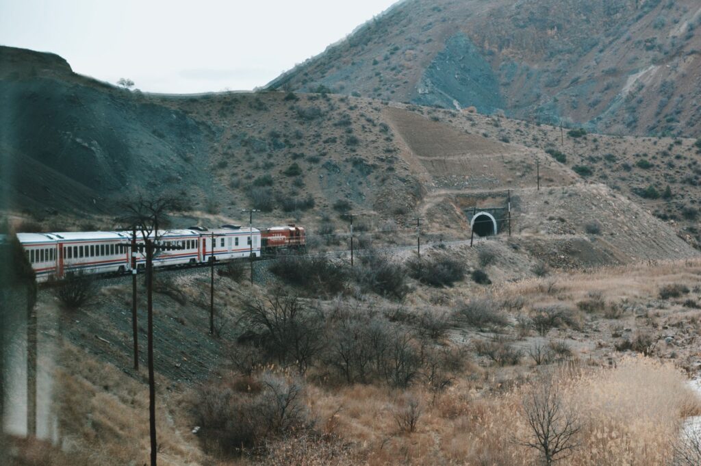 A scenic view of a train traveling through a mountainous landscape towards a tunnel.