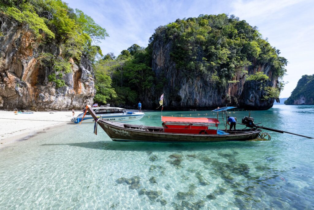 Peaceful Thai beach with clear waters, longtail boat, and limestone cliffs. A perfect tropical escape.