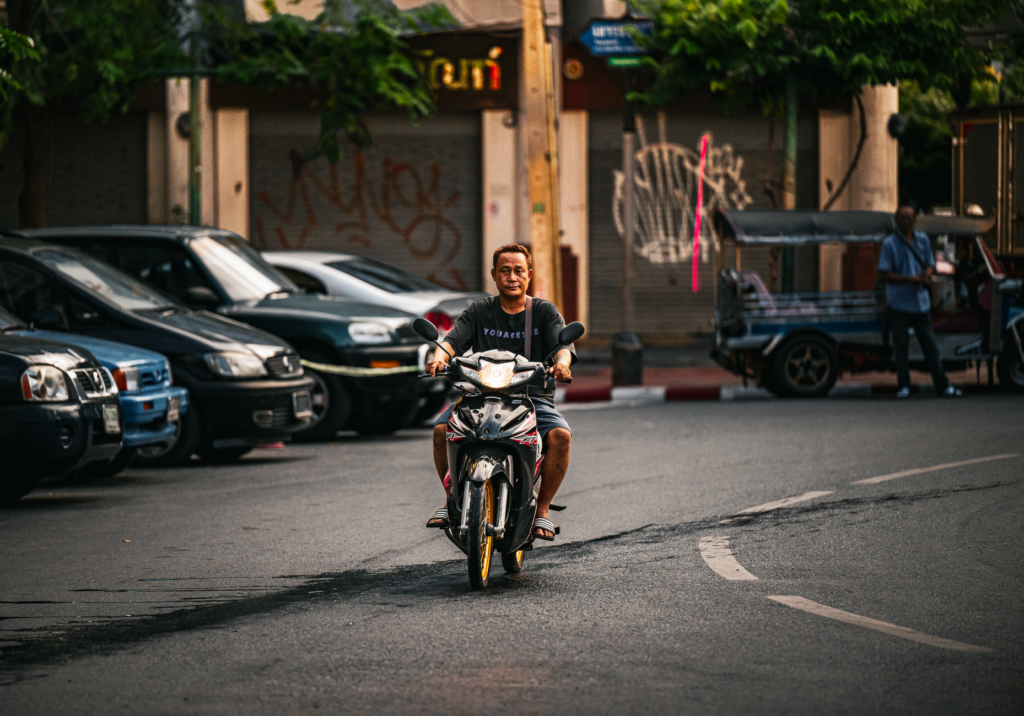 Casual street scene with a man riding a scooter in vibrant Bangkok.