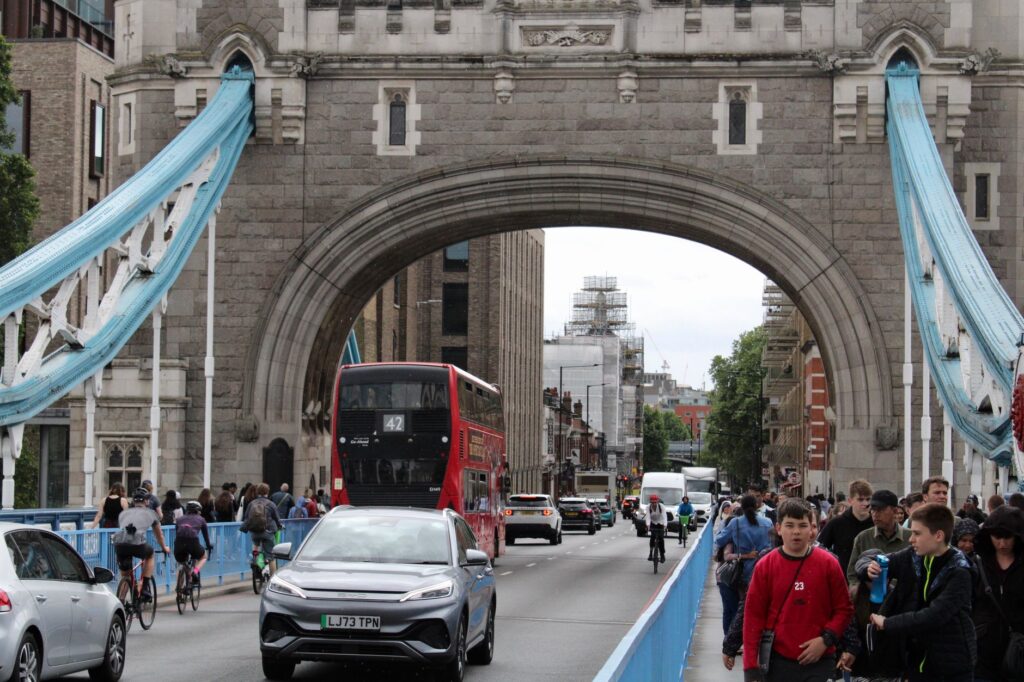 Crowds and traffic cross Tower Bridge in London, showcasing a busy urban scene.